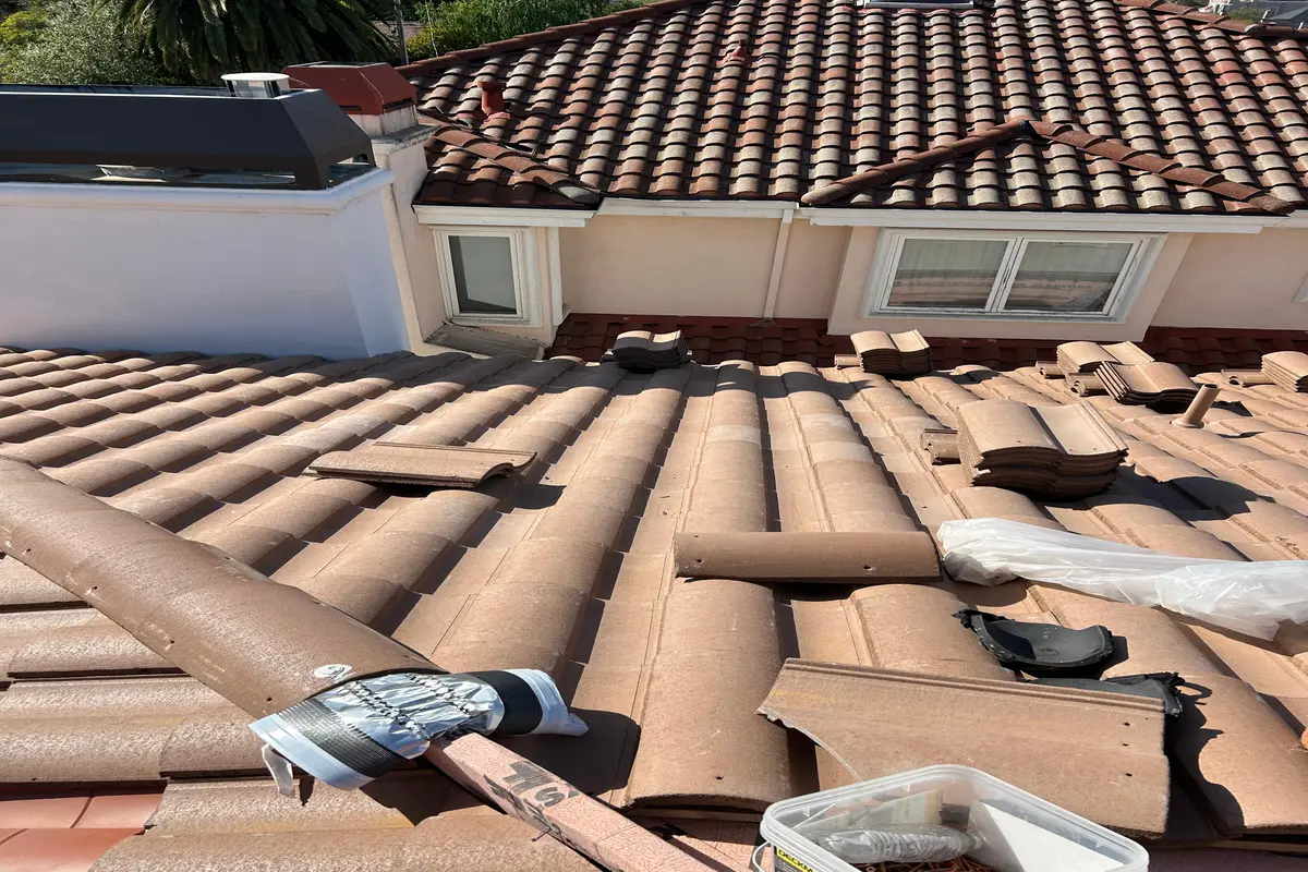 Concrete tile roof replacement in progress with tiles staged on new underlayment
